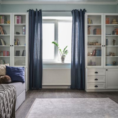 Light, cozy teen room with blue curtains, white shelving/drawers, beige area rug