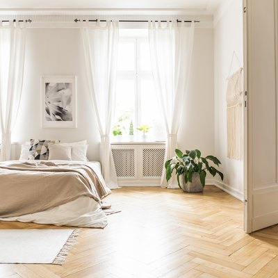 Bright bedroom with sheer white curtains, beige decorations, hardwood floor