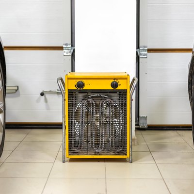 Big heavy industrial electric fan heater in double car garage interior. Two vehicles parked for winter storage in dry warm heating parking for cold winter season.