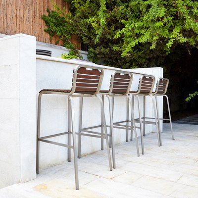 Four empty bar stool chairs with wooden seats and metal foot near a white concrete bar counter.