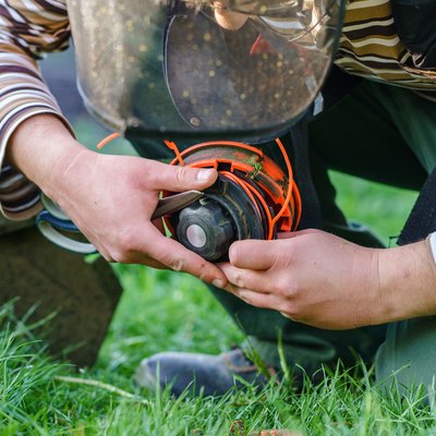 Close up on string trimmer head unknown caucasian man holding and repairing weed cutter replacing parts replacement in day on the field farmer or gardener