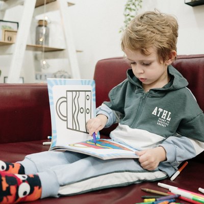 Boy sitting on couch drawing or coloring with markers.