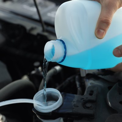 Man pouring antifreeze from plastic canister into windshield washer fluid reservoir, closeup