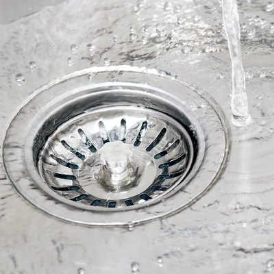 Water running from tap in a sink and pouring into drain with strainer stopper.