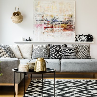 Patterned pillows on gray corner sofa in living room interior with table and painting. Real photo.