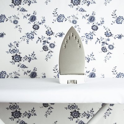 Iron on ironing board with wallpaper pattern in background