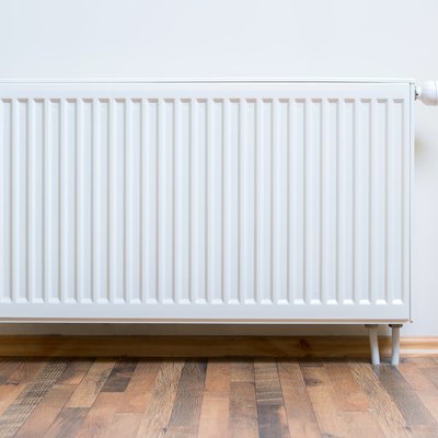 Home radiator heater on the white wall on wooden hardwood floor. Adjustable warming equipment for apartment and home