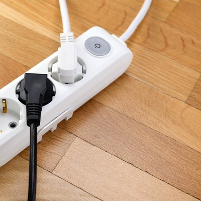 White power strip with three outlets on wooden floor. Power strip with switch for home or office.