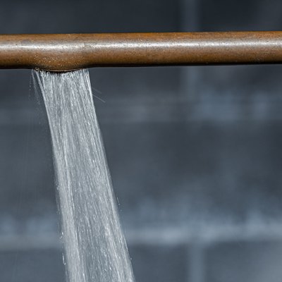 A close-up of a ruptured copper pipe spraying water against a basement wall