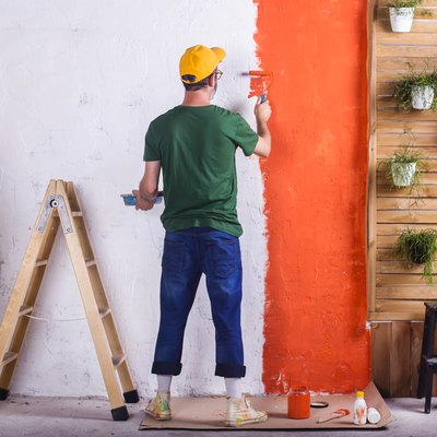 Rear view of man painting a wall orange in his garden terrace.