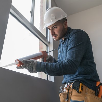 Building contractor installing a window and applying silicone sealant