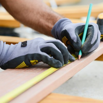 close up detail of manual worker hands working with a measuring tape and pencil in wood plank