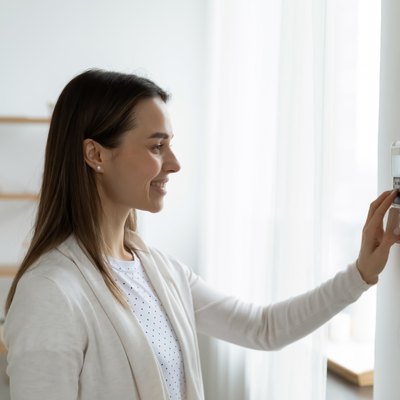 Smiling woman adjusting degrees set comfortable temperature using thermostat