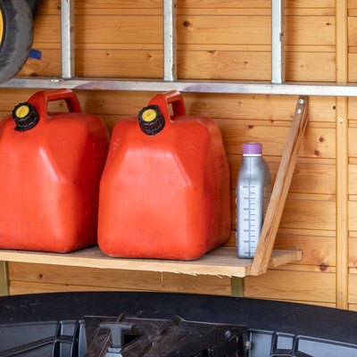 Garage corner with three red plastic fuel cans , staircase and snow plough for atv with wooden wall on background. Petrol gas containers reserves storage at vehicle home garage