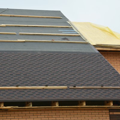 How to install asphalt roof shingles: A close-up of asphalt shingles installation on the roof covered with water-resistant underlayment without  fascia board and a roof sheathed with plywood.