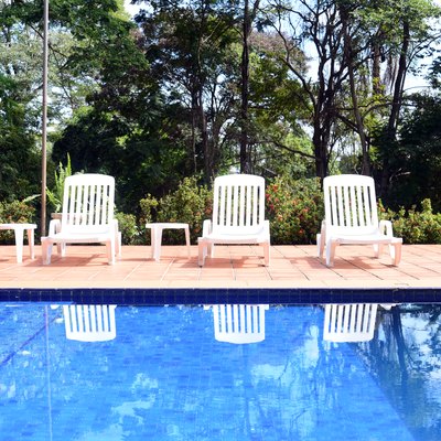 Pool with white chairs and a garden in the background.