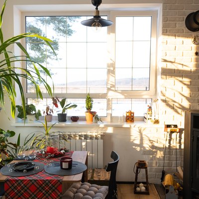 Sunny interior of a loft-style house with potted plants, a large window, a covered table for the Christmas and New Year holidays