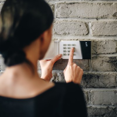 Young woman entering security pin on home alarm keypad.