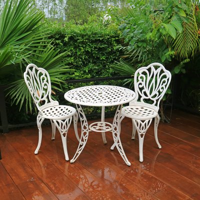 White wrought iron garden tea table and chairs on patio after rain.