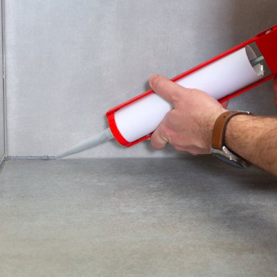 A plumber applies silicone sealant to the joining of ceramic tiles