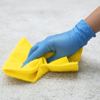 Person in blue gloves blotting a spill with a bright yellow cleaning cloth on white carpet.