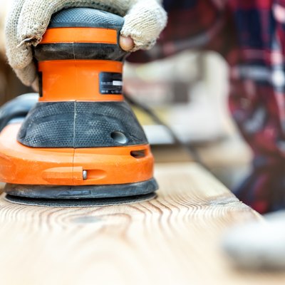 Closeup of carpenter grinding a wood plank with an orbital sander.