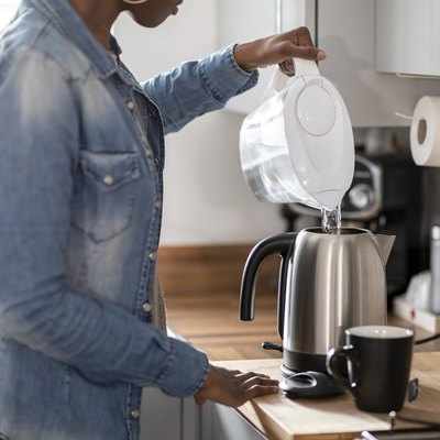 Woman pouring water into kettle in kitchen
