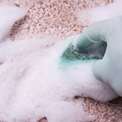 Cleaning carpet by hand with a sponge and foam cleaner.
