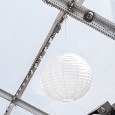 Closeup of hanging one white paper party ball or sphere light lantern from ceiling in restaurant building venue with fan, speakers
