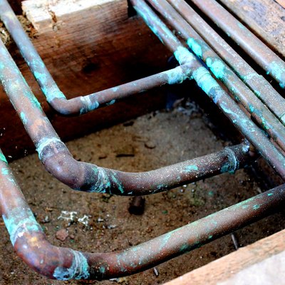 Closeup image of old copper pipes under floor.
