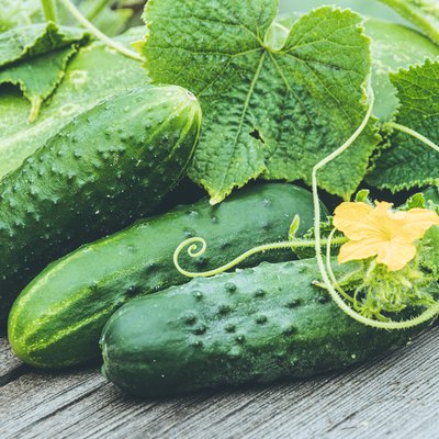 Fresh cucumbers with green leaves and flowers on wooden table.