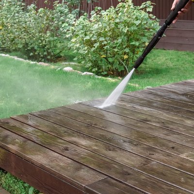 Cleaning a deck with high pressure power washer. Washing terrace wood planks and cladding walls.