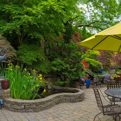 Home backyard hardscape and lush plants landscaping with garden furniture on paver brick patio.