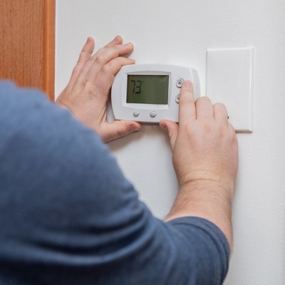 Man is pushing buttons and adjusting thermostat to change temperature at home