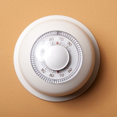 Round, white analog-dial thermostat on peach wall
