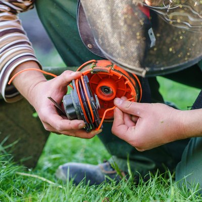 Close up on string trimmer head unknown caucasian man holding and repairing weed cutter replacing parts replacement in day on the field farmer or gardener