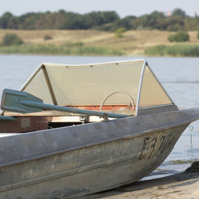 Old aluminum fishing boat by lake or river.