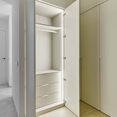 Opened door of lighted white wooden built-in wardrobe.