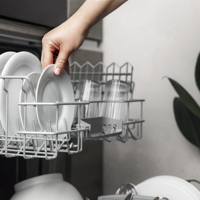 Open dishwasher with clean cutlery, glasses, dishes inside in home kitchen.