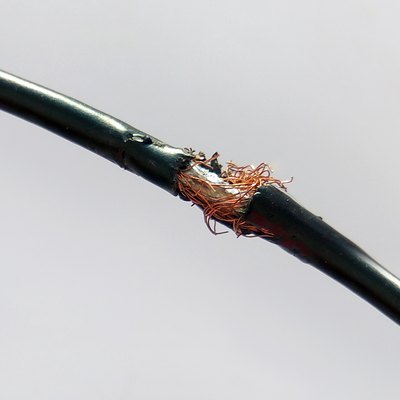 Damaged black electric cord on light background. Dangerous broken power electrical cable