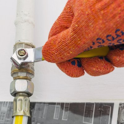 A gasman's hand in orange protective working gloves closes the gas valve.