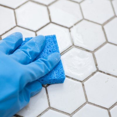 blue cleaning gloves holding a sponge cleaning a tile floor