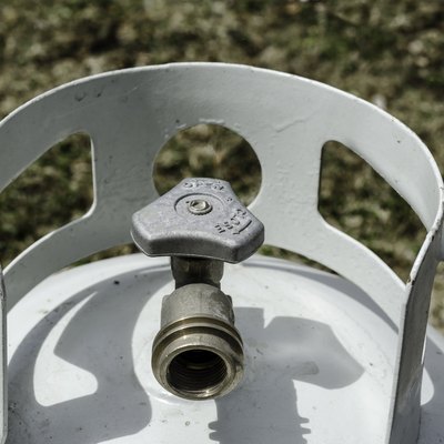 Angled overhead close-up of the top of a white propane tank and brass valve with grass in the background