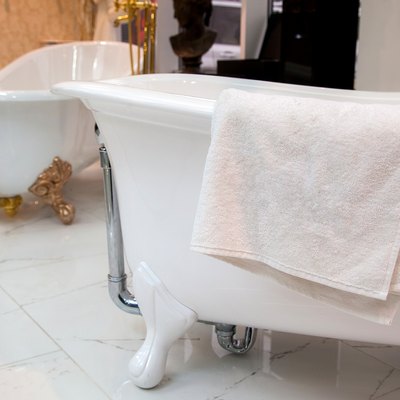 a white terry towel lies on a cast-iron bathtub on a ceramic tile floor in a store.
