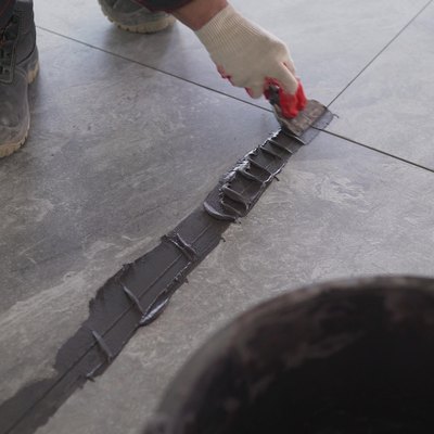 The hand of man holding a rubber float and filling joints with grout. A worker uses black grout to rub the gaps between the tiles on the floor. A worker is rubbing the tiles on the floor