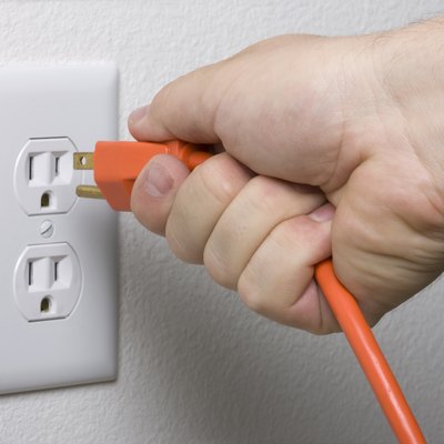 Unplugging an orange cord from a white electrical outlet.