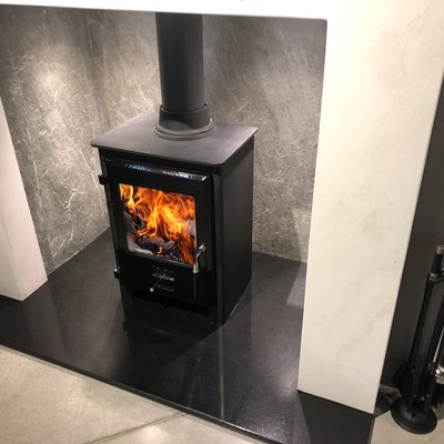 Image of square cast iron woodburner / contemporary log wood burning stove fireplace mantle with orange fire flames burning and generating heat to warm up room instead of gas boiler central heating, modern multifuel stove wood burner stand / chimney flue