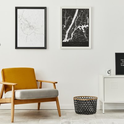 White retro living room with framed maps, designer armchair, lamp. Modern home decor.