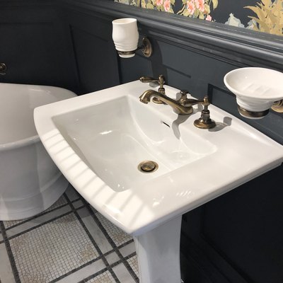 Image of luxury washroom bathroom with large freestanding bath with curved ends and bronze mixer tap, white rectangular sink wash basin with soap dish, wood panelling painted black and floral wallpaper with flowers pattern, mosaic tiled flooring tiles