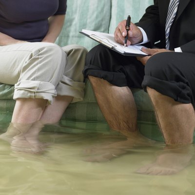 Mature man and mid adult woman sitting on sofa with water over their ankles, low section